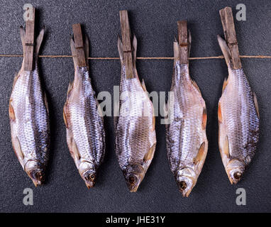 Getrockneter Fisch hängen an einem Seil auf schwarzem Hintergrund Stockfoto