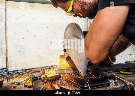 Ein junger Mann Schweißer schneidet ein Metall mit einer Kreissäge in der Werkstatt Stockfoto