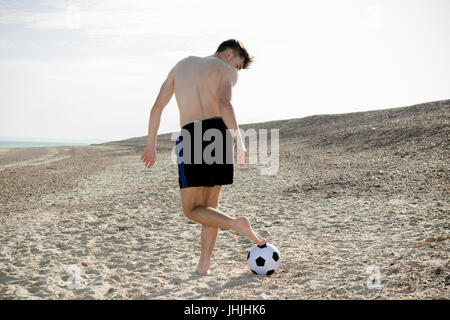 Teenager-Jungen spielen mit einem Fußball am Strand Stockfoto