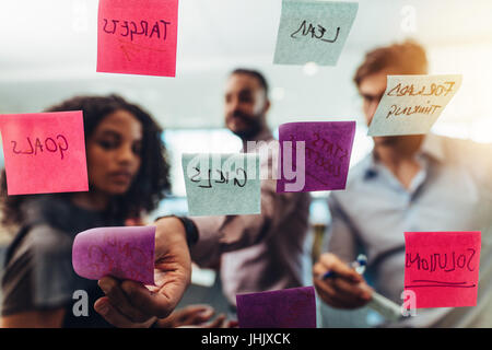 Geschäftsleute auf Notizzettel schreiben und klebt sie auf Glas im Amt. Bunte Klebezettel auf Glas mit Notings auf sie. Stockfoto