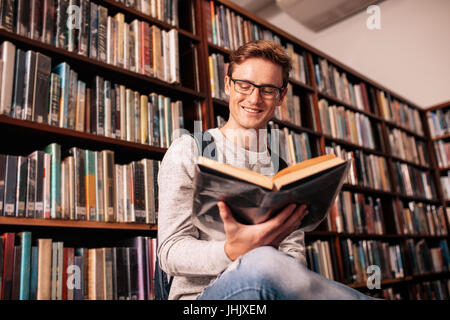 Kaukasischen Jüngling Buch zu lesen, während der Sitzung in der Universitätsbibliothek. Glücklich Universität Studierender in Bibliothek. Stockfoto