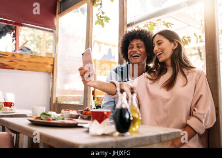 Stets gut gelaunte Frau nehmen Selfie mit ihrer Freundin im Café. Paare, die Spaß mit Smartphone im Coffee Shop Stockfoto