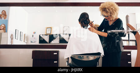 Friseur styling der Haare eines Kunden im Salon. Weibliche Stilist Einstellung Haare in modischem Design mit einem Kamm. Stockfoto