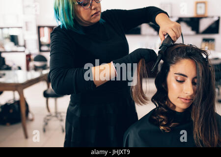 Frau bekommen eine Frisur im Salon. Friseur, glattes Haar in locken mit einem Lockenstab Haar verwandeln. Stockfoto