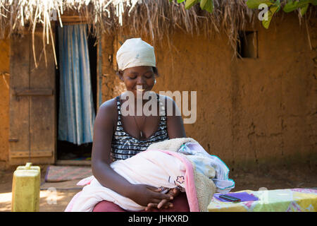 Eine Mutter mit ihrem Neugeborenen Baby außerhalb ihrer traditionellen Lehmhütte zu Hause in Bukeeri, Uganda. Stockfoto