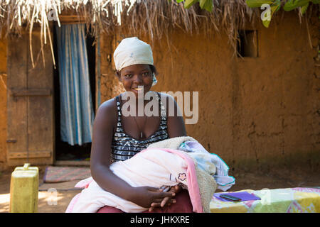 Eine Mutter mit ihrem Neugeborenen Baby außerhalb ihrer traditionellen Lehmhütte zu Hause in Bukeeri, Uganda. Stockfoto
