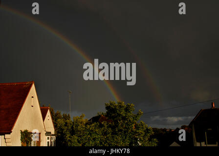 Doppelter Regenbogen und dunkle Wolken über Vorstadthäuser Stockfoto