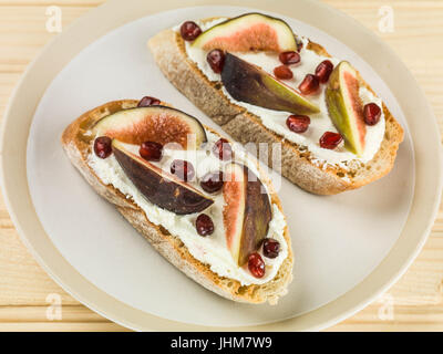 Weicher Ricotta-Käse mit Feigen und Granatapfel Samen auf geröstetem Ciabatta-Brot auf einem Teller Stockfoto