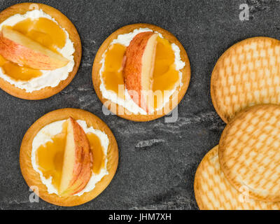 Weicher Ricotta-Käse mit Apfel und Honig auf einem Keks oder Cracker vor schwarzem Hintergrund Stockfoto