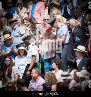 Wimbledon, London, UK. 14. Juli 2017. Die Wimbledon Tennis Weltmeisterschaften 2017 statt auf The All England Lawn Tennis and Croquet Club, London, England, UK.    Herren Einzel - Halbfinale Sam Querrey (USA) [24] V Marin Cilic (CRO) [7] auf dem Centre Court.  Tie-Break-Spiel wird angehalten, während Lady Zuschauer unwohl getroffen wird.  Gallant Stewards escort sanft die unglückliche Dame neben dem Platz, so dass sie ärztliche Hilfe erhalten kann. Stockfoto