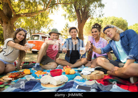 Porträt von lächelnden Freunde zeigen Bierflaschen und Gläser beim Sitzen auf Feld bei Picknick Stockfoto