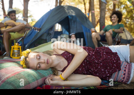 Frau schläft während Freunde sitzen im Hintergrund auf Campingplatz Stockfoto