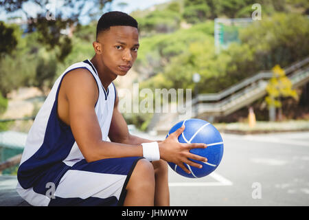 Porträt von Teenager mit Basketball sitzen auf Bank vor Gericht Stockfoto