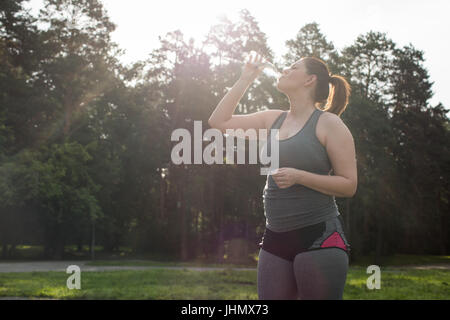 Verschwitzte übergewichtige Frau trinkt Wasser nach einem langen Training. selektive Fokus Stockfoto