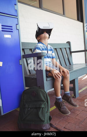 Junge mit virtual-Reality-Brille sitzend auf Bank im Flur in der Schule Stockfoto