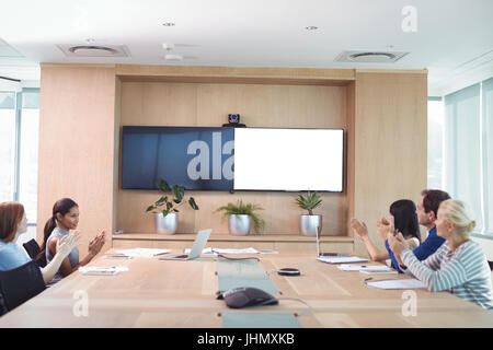 Geschäftsleute, die während der Sitzung im Sitzungssaal Händeklatschen Stockfoto