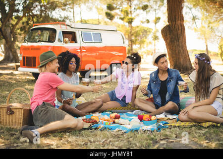 Freunden Picknick beim Sitzen gegen Wohnmobil auf Feld Stockfoto