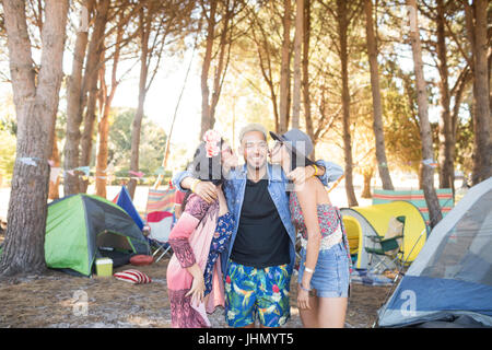 Frauen küssen männlichen Freunde stehen auf Feld auf Campingplatz Stockfoto
