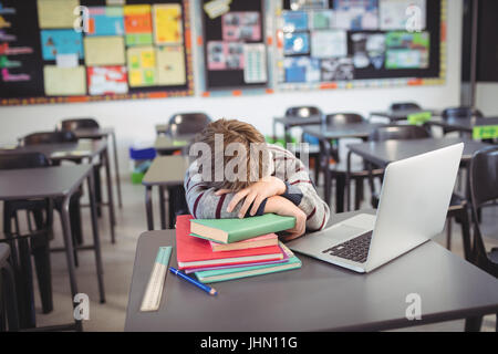 Müde Schüler schlafen auf Stapel des Buches per Laptop im Klassenzimmer Stockfoto