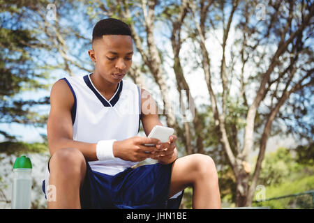 Teenager mit Smartphone beim Sitzen auf der Bank vor Gericht Stockfoto