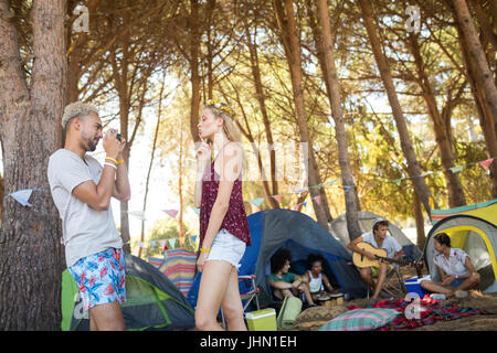 Seitenansicht des Lächelns Mann Fotografieren Freundin mit Freunden im Hintergrund auf Campingplatz Stockfoto