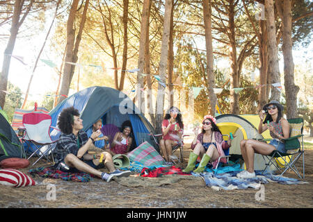 Junge Freunde sitzen zusammen Zelten auf Feld auf Campingplatz Stockfoto