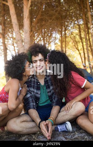 Frauen küssen Junge männliche Freunde sitzen auf Feld auf Campingplatz Stockfoto