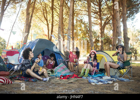 Junge Freunde, die gemeinsam von Zelten auf Feld auf Campingplatz Stockfoto