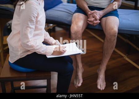 Vogelperspektive Ansicht weiblichen Therapeuten schreiben in Zwischenablage beim Sitzen durch senior männlichen Patienten im Krankenhaus Stockfoto
