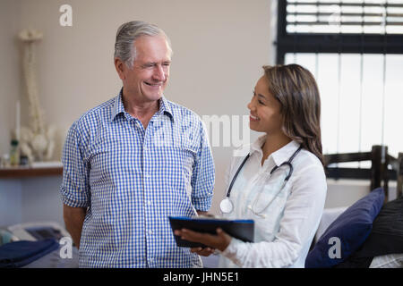 Lächelnd senior männlichen Patienten und weiblichen Therapeuten diskutieren Datei auf Krankenstation Stockfoto