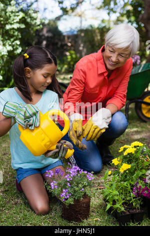 Lächelnd senior Frau betrachten Mädchen Blumen im Garten gießen Stockfoto