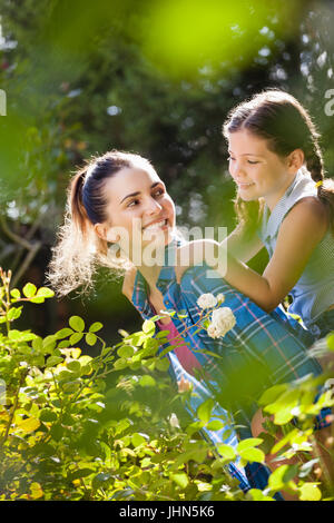 Lächelnde Mutter geben Huckepack Fahrt, Tochter von Pflanzen im Garten auf sonnigen Tag Stockfoto