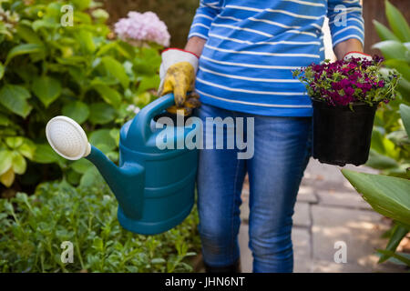 Mittelteil senior Frau mit Gießkanne und Blumentopf inmitten von Pflanzen im Garten Stockfoto