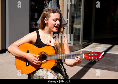 Eine junge Studentin Straßenmusikant Gitarre spielen und singen, etwas Geld in Dundee, Großbritannien Stockfoto