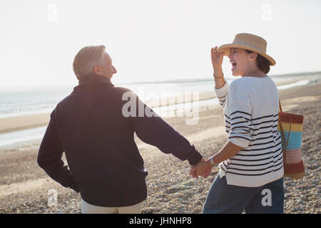 Älteres Paar Hand in Hand und Wandern am sonnigen Strand lachen Stockfoto