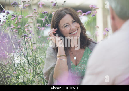 Lächelnde Reife Frau im Gespräch mit Menschen auf der Terrasse mit lila Blüten Stockfoto