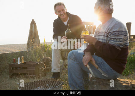 Senioren Herren Wein trinken und Grillen am Sonnenuntergang Strand Stockfoto