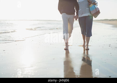 Liebevolle barfuß älteres Paar gehen, Hände halten in sonnigen Strand-Brandung Stockfoto