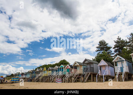 Bunte, hölzerne Strandhütten auf Stelzen an der verlassenen sandigen Strand des Wells nächsten Meeres in Nirfolk, Großbritannien unter blauem Himmel mit Sonne im Sommer. Stockfoto