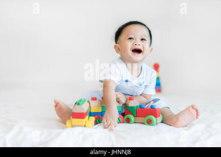 Entzückende asiatische Baby junge 9 Monate am Bett sitzen und spielen mit Farbe Holzeisenbahn Spielzeug zu Hause. Stockfoto