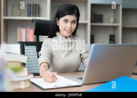 Asiatische junge intelligente Frau Manager mit lässig ihr Geschäft Arbeit mit Laptop und sitzen auf Stuhl in Manager-Zimmer. Stockfoto