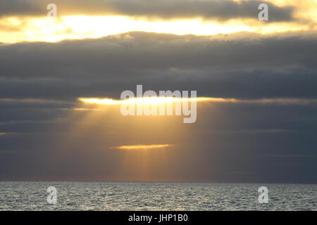 Durch Wolken über Meer aufgehende Sonne Stockfoto