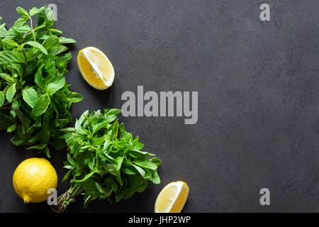 Frische Minze Basilikum Bündel und Zitronen auf dunklem Schiefer Tafel Hintergrund. Ansicht von oben. Zutaten für Sommer erfrischenden Drink cocktail Stockfoto