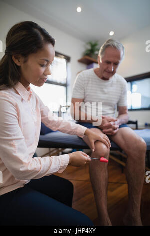 Weiblichen Therapeuten untersuchen Knie senior männlichen Patienten mit Reflexhammer auf Krankenstation Stockfoto