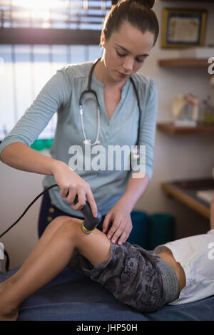 Junge weibliche Therapeuten mit Ultraschallgerät am Knie des jungen Spitalabteilung Stockfoto