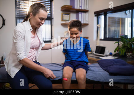 Junge weibliche Therapeuten untersuchen junge mit Reflexhammer auf Knie beim Sitzen auf dem Bett in der Krankenstation Stockfoto