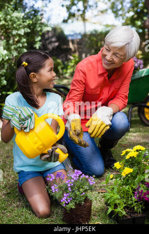 Fröhlichen senior Frau betrachten Mädchen Blumen im Garten gießen Stockfoto