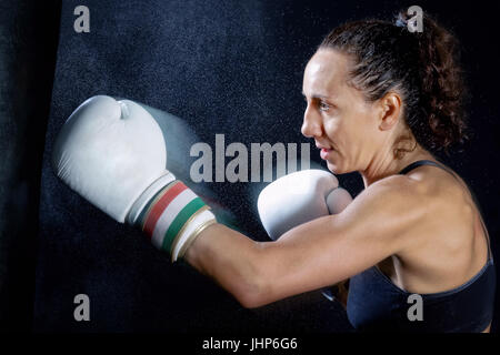 Eine Boxer Frau wirft einen Schlag in der Plünderung. Spritzer von Wasser und Schweiß auf dem schwarzen Hintergrund. Stockfoto