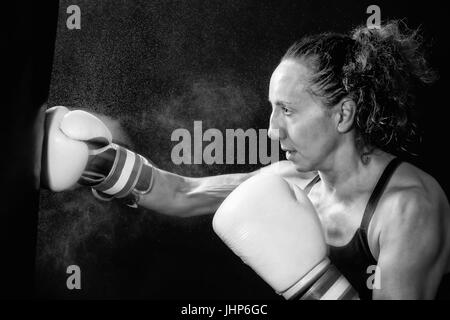 Eine Boxer Frau wirft einen Schlag in der Plünderung. Spritzer von Wasser und Schweiß auf dem schwarzen Hintergrund. Stockfoto