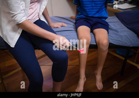 Geringer Teil der weiblichen Therapeuten untersuchen junge mit Reflexhammer auf Knie im Krankenhaus Stockfoto
